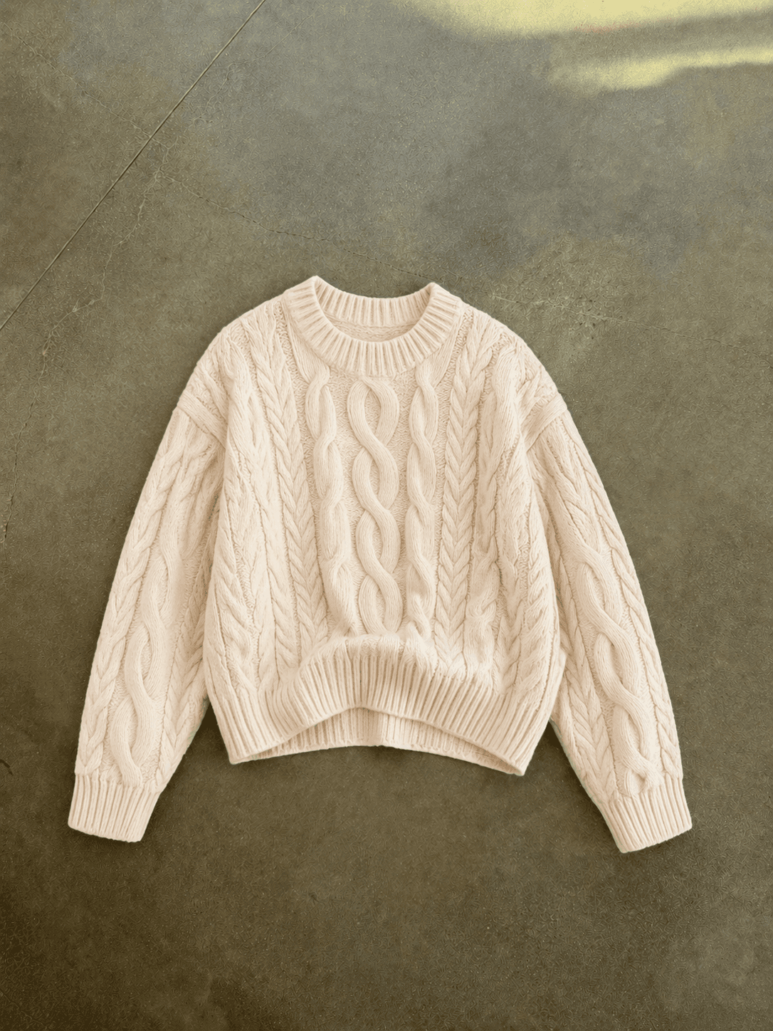 Beige cable knit sweater on a textured brown background