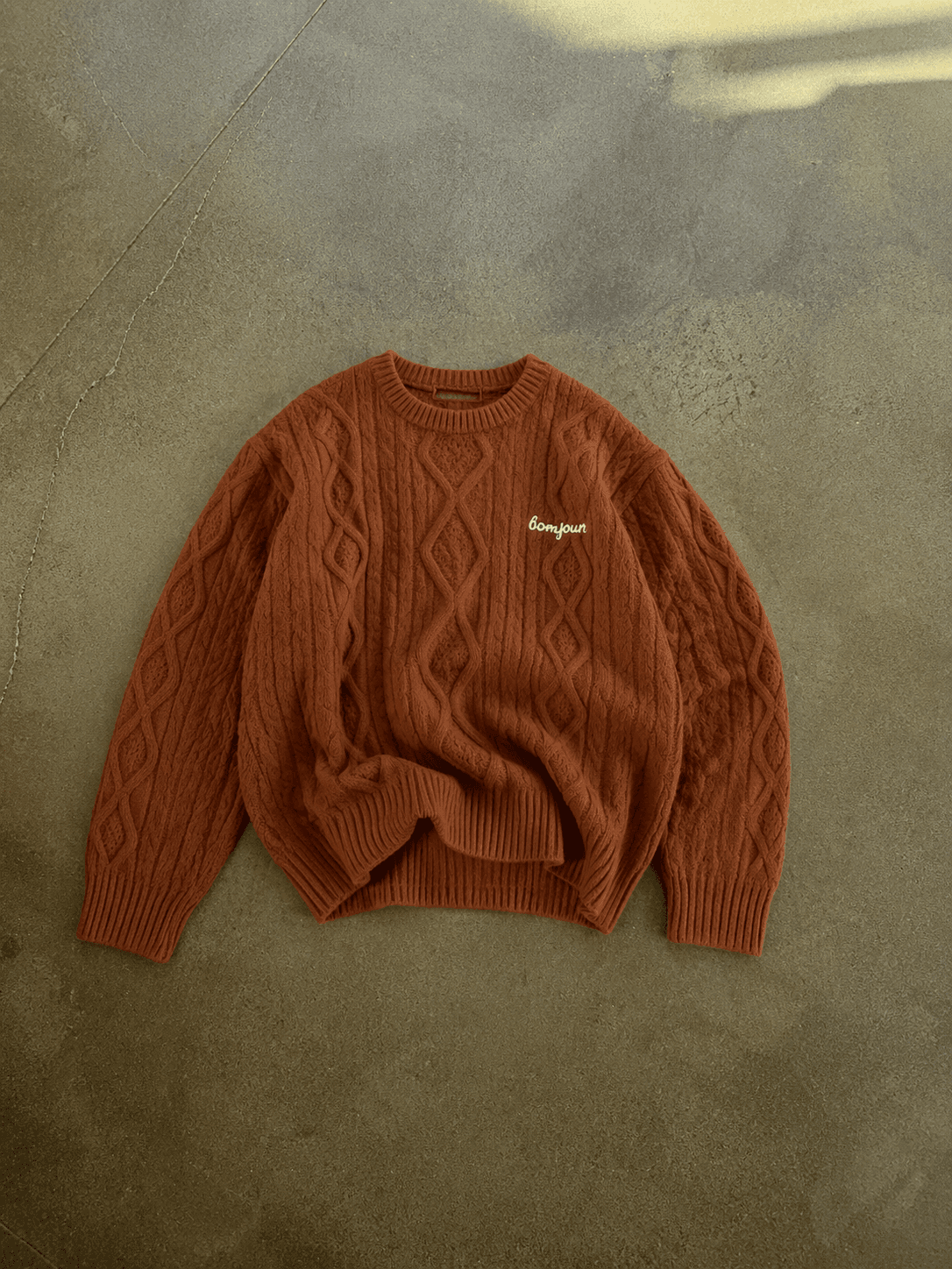 Brown cable knit sweater with a brand logo on a concrete floor