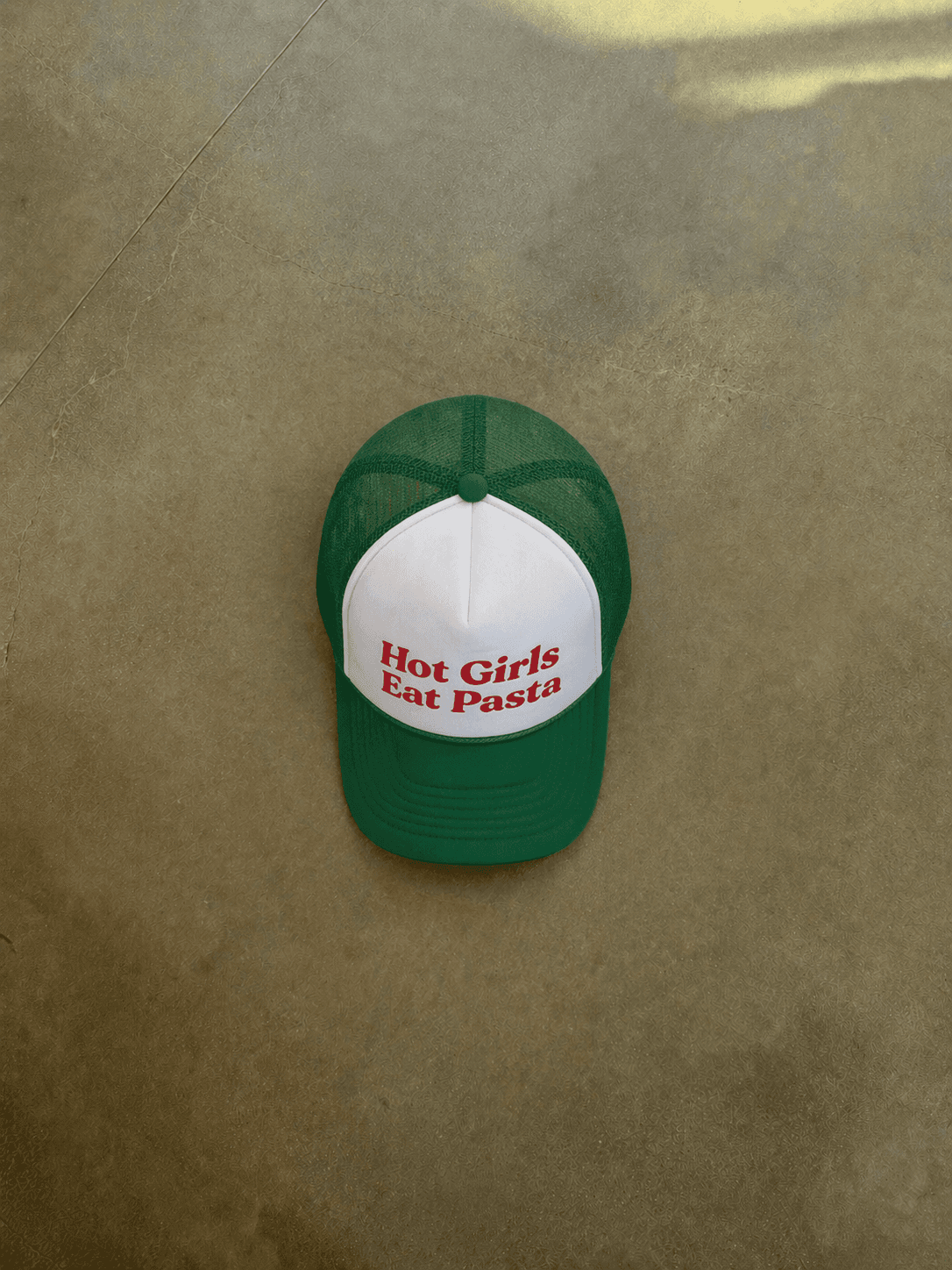 Green and white cap with 'Hot Girls Eat Pasta' text on a brown surface