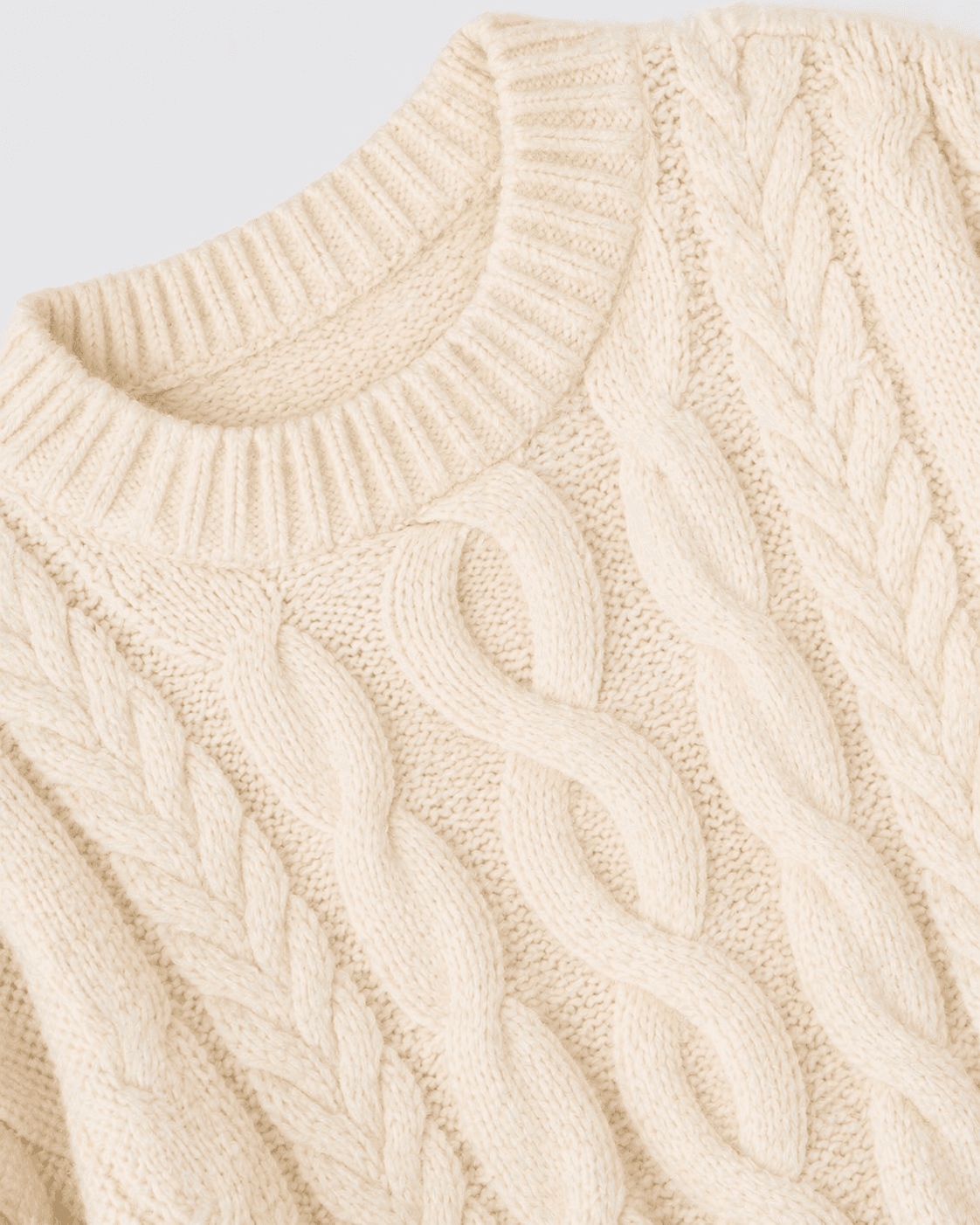 Close-up of a cream-colored cable knit sweater on a light gray background