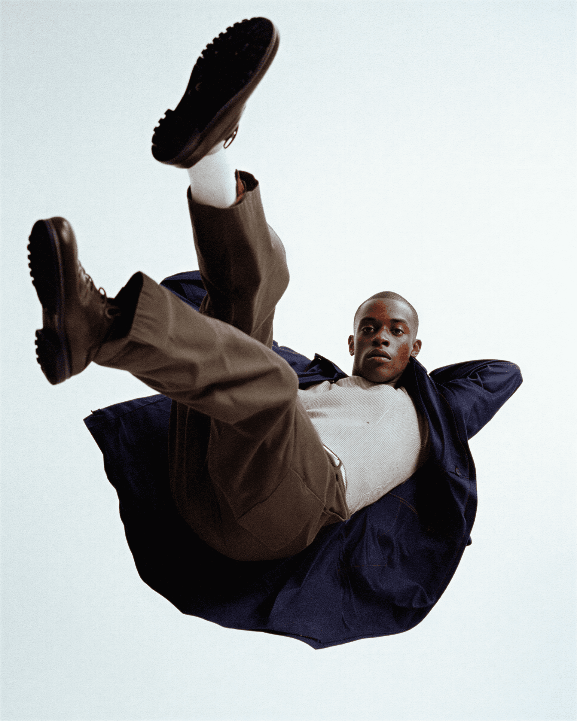Person in a dark coat and brown pants falling or floating against a light background
